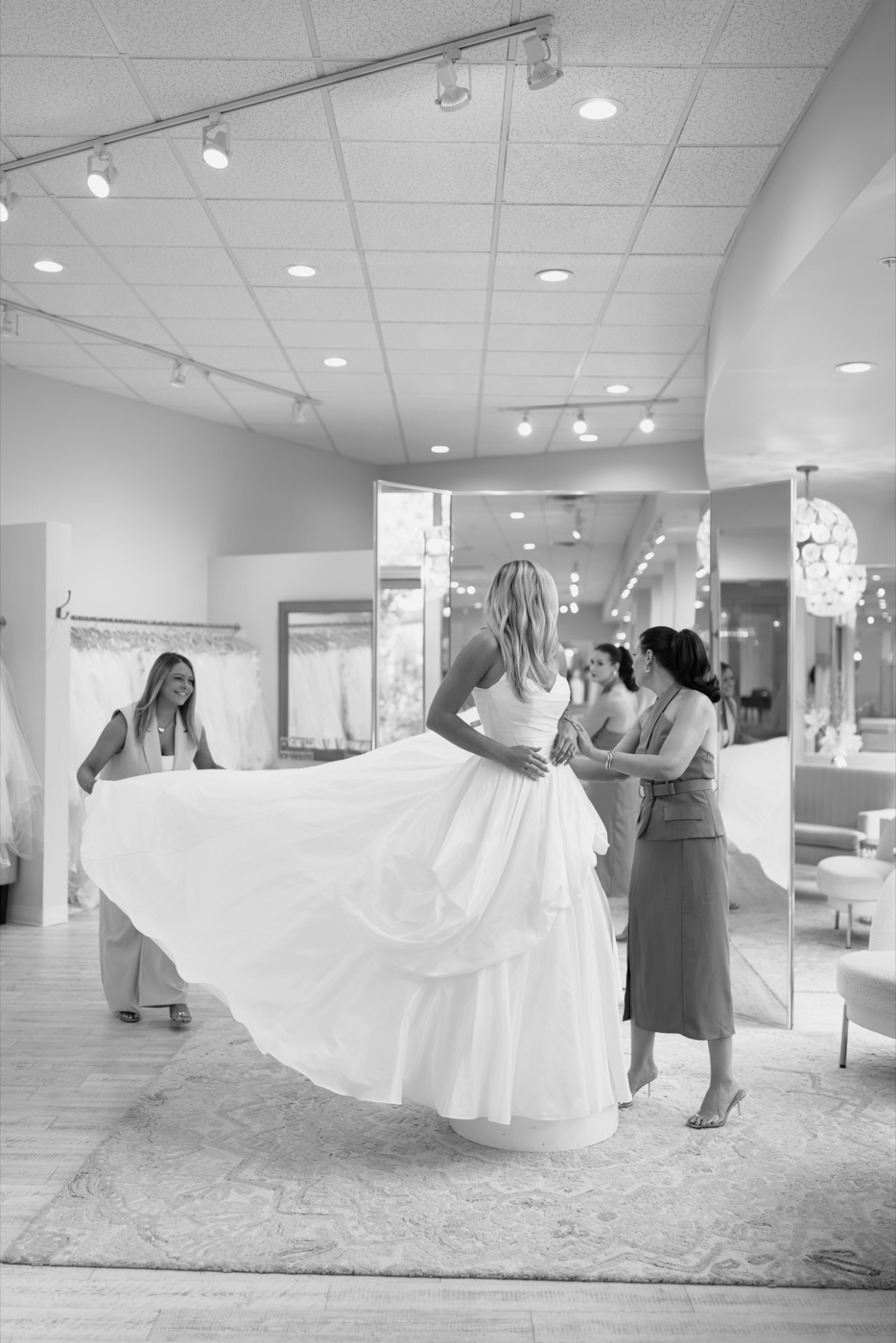 Bride with her train being arranged by a consultant near a window