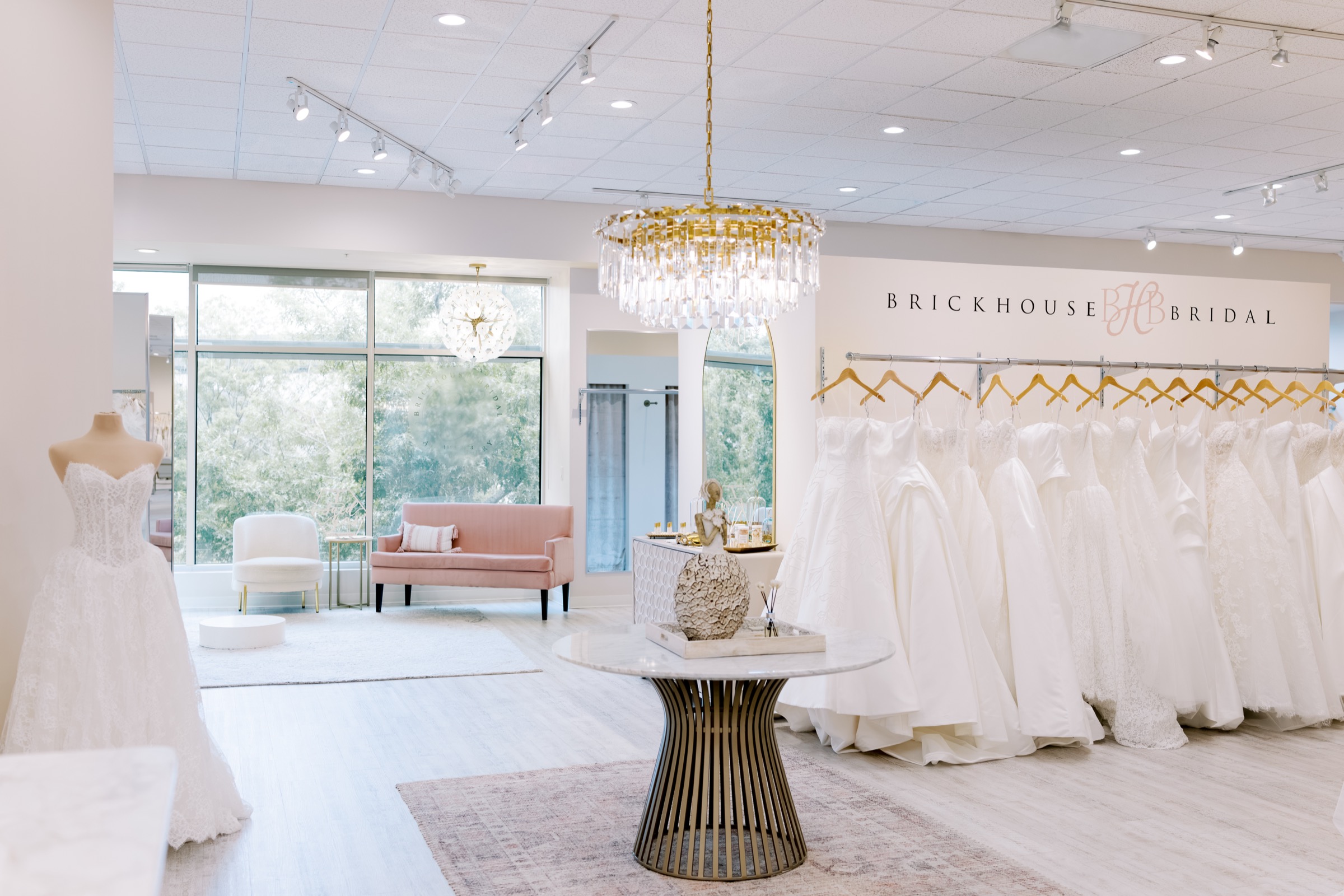 Bright, airy Brickhouse Bridal showroom in The Woodlands, Texas, lined with wedding gowns and a crystal chandelier