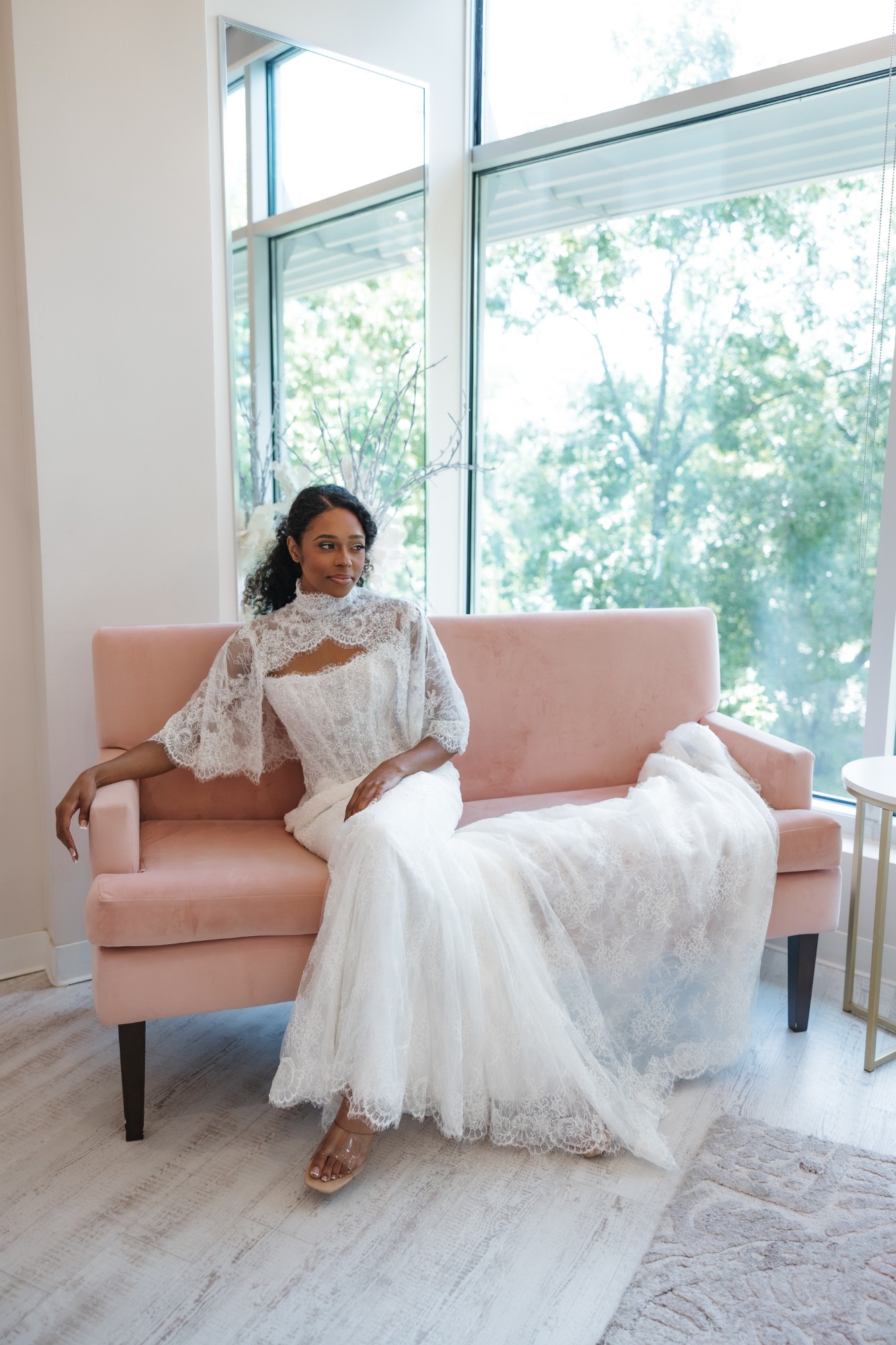 Bride in Martina Liana ML2010 with detachable lace cape seated on a pink velvet sofa